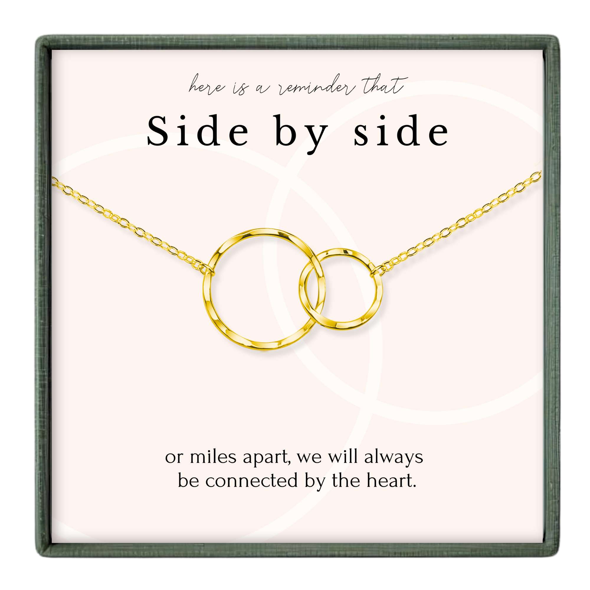 a necklace with two interlocking gold rings, accompanied by a message that reads "here is a reminder That Side by side or miles apart, we will always be connected by the heart."
