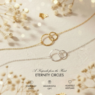 a necklace with two intertwined rings, symbolizing the connection between two hearts. The necklace is displayed on a white background, with delicate white flowers and a blurred background, creating a serene and elegant atmosphere.