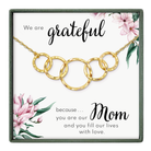 The image is a necklace with a pendant that says "We are grateful because... Mom" and features a floral design.