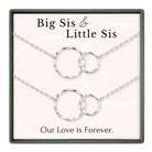 a set of two silver necklaces with interlocking circular pendants, accompanied by the text "Big Sis & Little Sis" and "Our Love is Forever."