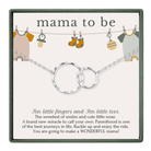 The image is a gift box for a baby shower, featuring a necklace with two silver rings and baby clothes hanging on a clothesline.