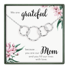 The image is a necklace with a pendant, featuring a floral design and a message about being a mother.