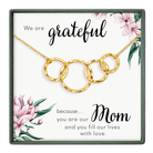 The image is a necklace with a pendant that says "We are grateful because... Mom" and features a floral design.
