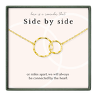a necklace with two interlocking gold rings, accompanied by a message that reads "here is a reminder That Side by side or miles apart, we will always be connected by the heart."