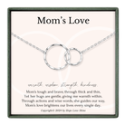 The image is a necklace with two interlocking silver rings, and it is presented in a square frame with a pink background.