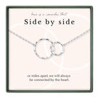 a necklace with two interlocking silver rings, accompanied by a message that reads "here is a reminder That Side by side or miles apart, we will always be connected by the heart."