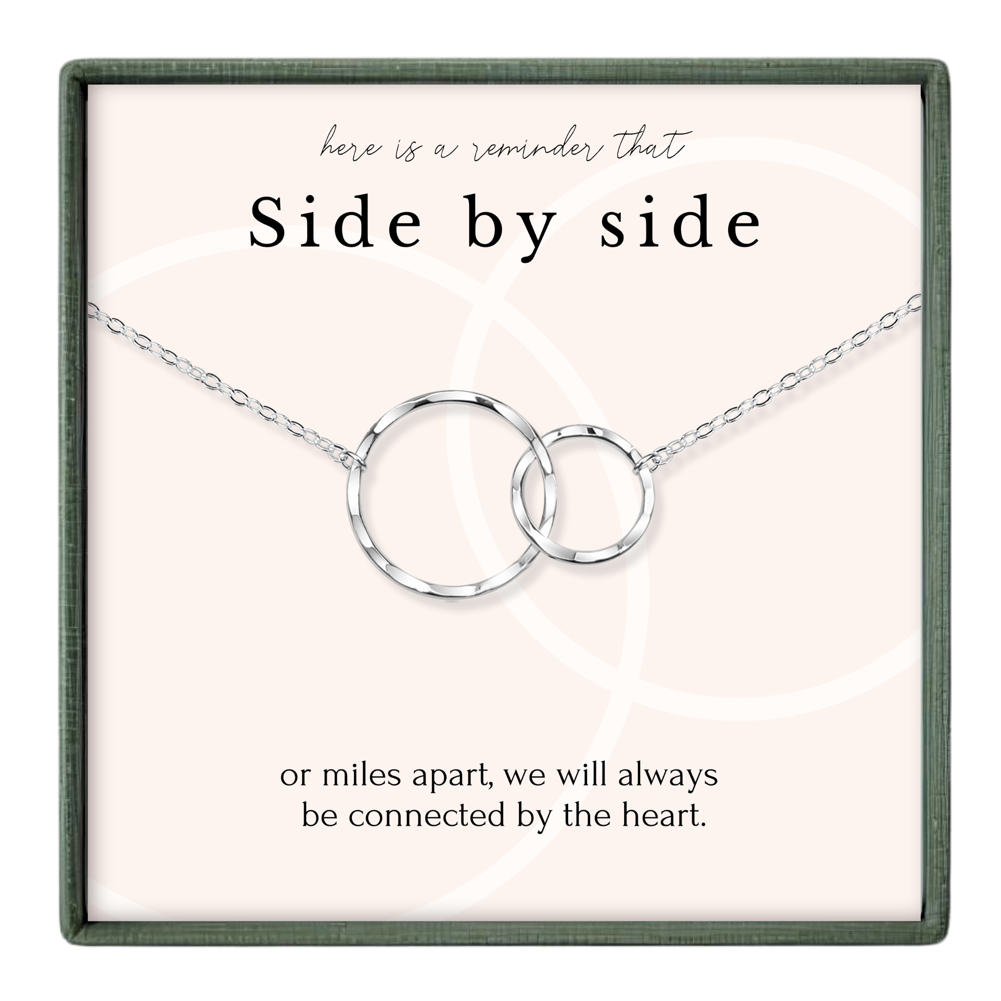 a necklace with two interlocking silver rings, accompanied by a message that reads "here is a reminder That Side by side or miles apart, we will always be connected by the heart."