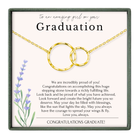 The image is a graduation gift box with a congratulatory message for a graduate. The box is framed in green and contains a gold chain with two circular pendants. The message congratulates the graduate on their achievements and wishes them a bright future.