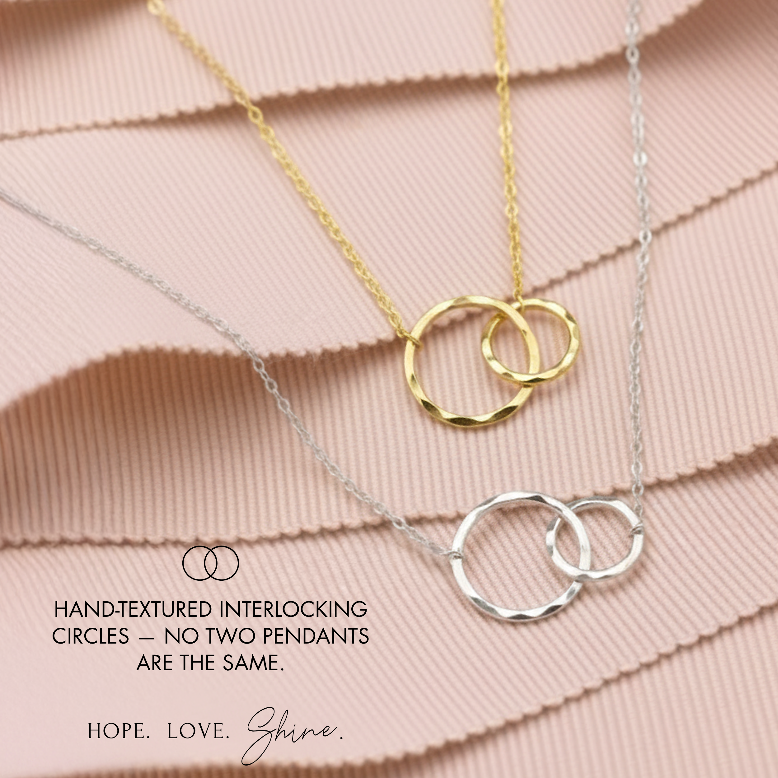 a necklace with two interlocking rings, one gold and one silver, set against a pink fabric background.