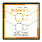 The image is a necklace set with two circular pendants, each with a chain. The text above the necklace reads "YOU ARE MY SUNSHINE." Below the necklace, there is a message that says "MY ONLY SUNSHINE, YOU MAKE ME HAPPY WHEN SKIES ARE GRAY."