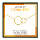 The image is a necklace with two gold rings, and it is presented in a box with a message that reads "You are my sunshine."