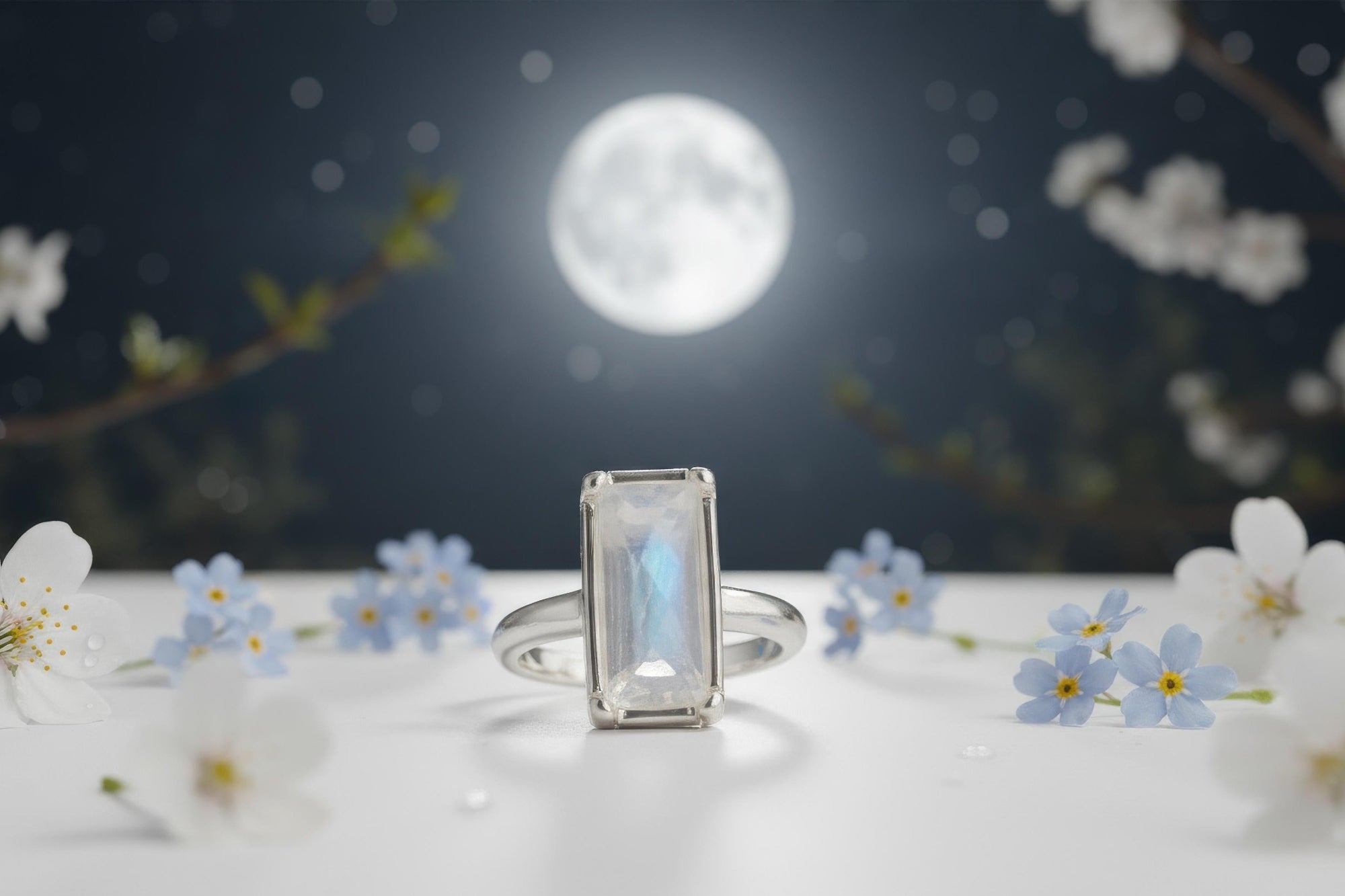 moonstone Ring with a rectangular gemstone on a surface with flowers and a moonlit background